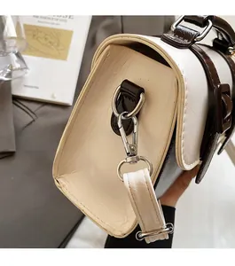 Detail of silver metallic clasp and brown leather handle on a cream satchel bag