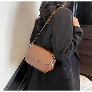 Close-up of brown leather crossbody bag with flap and metal buckle on black blazer