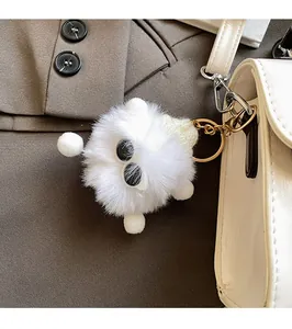 Detail of white plush doll charm with large eyes and gold clasp on a leather handbag