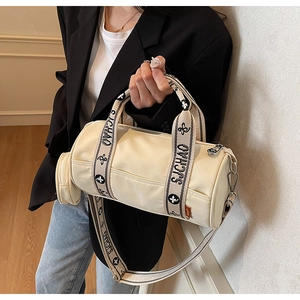 Détail du sac cylindrique en toile crème avec un petit porte-monnaie rond et bandoulière lettrée