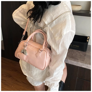 Pink glossy leather bowling bag shown on model with shoulder strap and heart charm