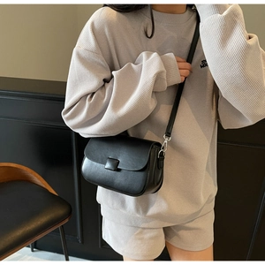 Detail of a minimalist black leather crossbody bag with square buckle on a model wearing grey set