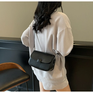 Detail of a minimalist black leather crossbody bag with a square buckle on a female model