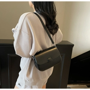 Detail shot of a minimalist black leather crossbody bag featuring a square closure buckle