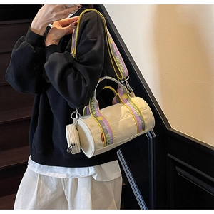 Détail porté d'un sac cylindrique en toile beige avec sangle jacquard et petite pochette
