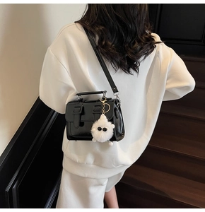 Detail of a black leather square bag featuring a cute white plush monster keychain charm
