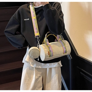 Détail d'un sac tonneau en toile blanc cassé avec une large bandoulière colorée et logo