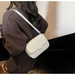 Side view of a white vintage soft leather crossbody bag worn by a model in a minimalist room
