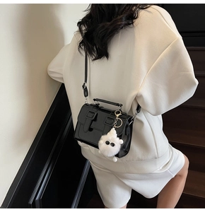 Detail of glossy black satchel with decorative buckles and a white plush monster pendant