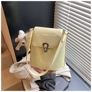 Détail du sac seau en cuir verni jaune clair avec fermoir en U argenté et breloque peluche