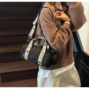Détail d'un sac cylindrique noir avec bandoulière tissée à motifs et petit porte-monnaie