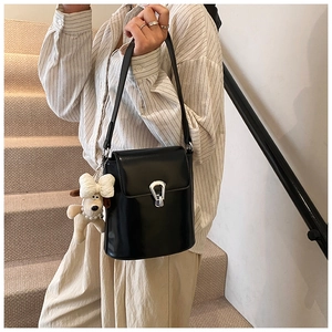 Détail du sac seau noir brillant avec boucle argentée et charm de petit chien en peluche blanc