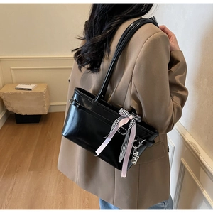 Détail d'un sac bandoulière noir brillant avec nœud à carreaux et breloque ours sur modèle