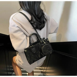 Sac à main noir texturé avec petit porte-monnaie rond porté par une femme chic