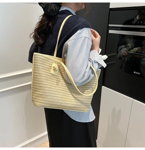 Détail d'un sac cabas en paille tressée beige avec de fines bandoulières porté par un mannequin