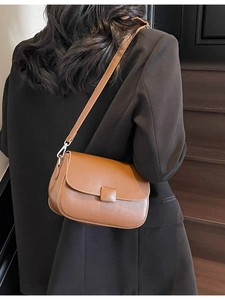 Brown vintage leather shoulder bag with square buckle worn with a black business blazer