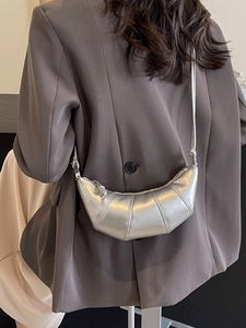 Metallic silver croissant crescent bag in crossbody style worn on dark suit