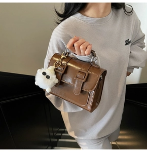 Close-up of a brown glossy leather satchel bag with stylish plush pendant and buckle straps