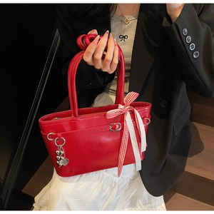 Détail d'un sac bandoulière en cuir verni rouge avec nœud à carreaux et pendentif cœur
