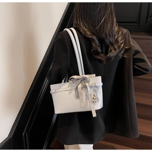 Détail d'un sac cabas gris clair avec breloque cœur et nœud porté par un mannequin