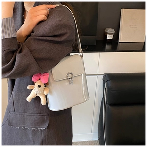 Détail du sac seau crème en cuir verni avec boucle argentée et pendentif chiot mignon