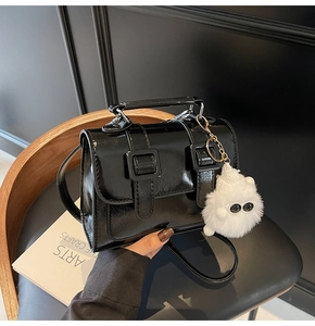 Close-up of a black patent leather mini crossbody bag with a white plush monster charm