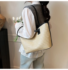 Détail d'un grand sac cabas en paille avec bandoulières en cuir noir sur l'épaule