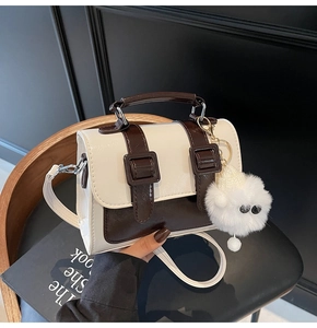 Detail of cream and brown retro satchel with decorative leather straps and plush charm