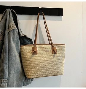 Détail du sac cabas en paille beige avec poignées en cuir marron nouées sur un cintre