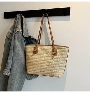 Détail du sac cabas en paille tressée avec bandoulière en cuir marron et détails noués