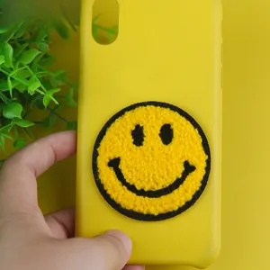 Detailed plush towel-embroidered smiley face patch on a vibrant yellow smartphone case