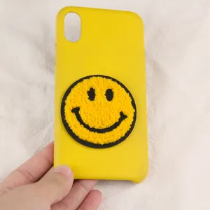 Detail of yellow phone case featuring a large fuzzy smile face embroidery patch