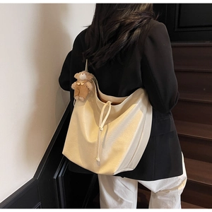 Detalle del bolso tote crema con cordón decorativo y colgante de oso marrón
