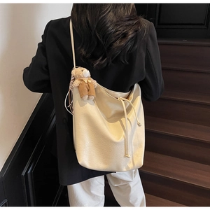 Detalle de un bolso tote beige minimalista con un colgante de oso de peluche en el lateral