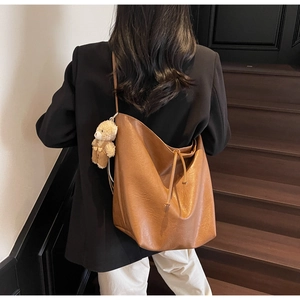 Detalle del bolso tote marrón caramelo con correas finas y colgante de oso de peluche