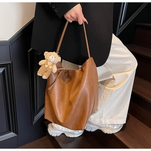 Detailed view of brown leather tote bag featuring a cute teddy bear plush charm