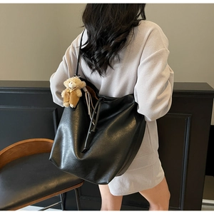 Detalle de un bolso tote negro de gran capacidad con colgante de oso y cordones