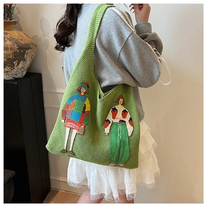 Detailaufnahme einer grünen Stricktasche mit Cartoon-Stickerei an der Schulter der Frau