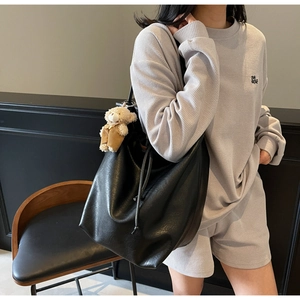 Close-up of large black soft leather tote bag featuring a cute brown bear doll charm