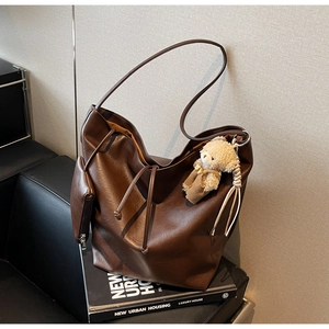 Detalle de un bolso hobo de cuero marrón con cordón, colgante de oso y estuche interior