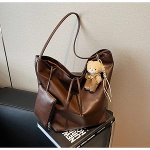 Close-up of brown faux leather tote with drawstring, bear charm and mini pouch