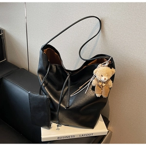Detalle de bolso tote negro con cordón ajustable y colgante de osito de peluche