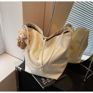 Detalle de un bolso tote de cuero blanco crema con cordón y un colgante de osito