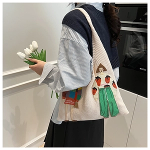 Detail der beigen Stricktasche mit bunter Illustration getragen an einer Schulter