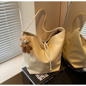 Detalle del bolso tote minimalista blanco roto con un colgante de oso junto a una ventana