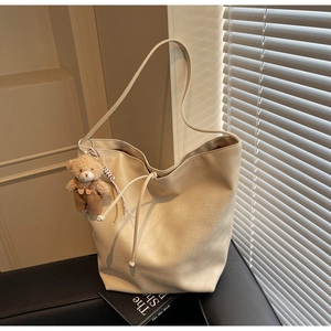 Detalle de un bolso tote crema grande con textura de cuero y colgante de osito