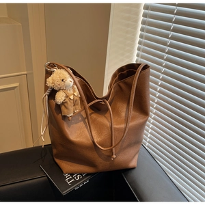 Detailed view of caramel brown leather tote bag texture with a cute teddy bear charm