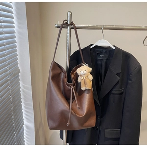 Detalle de un bolso tote de cuero marrón oscuro con textura suave y colgante de oso