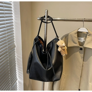 Detalle del bolso tote de cuero negro con cierre de cordón y colgante de oso lindo