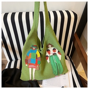Nahaufnahme der grünen Stricktasche mit Stickerei auf einem gestreiften Stuhlhintergrund